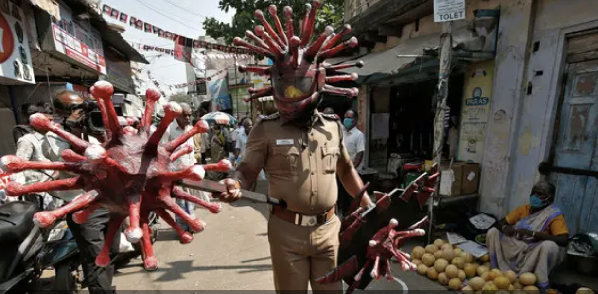 A police officer wearing a helmet and holding a shield molded to resemble the coronavirus patrols a market in Chennai.